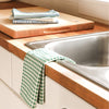 Kitchen sink area with wooden countertop, cutting boards, and green checkered towel.
