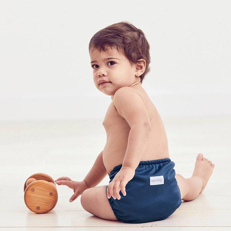 A baby playing with toys on the floor and wearing an Esembly diaper in dark navy