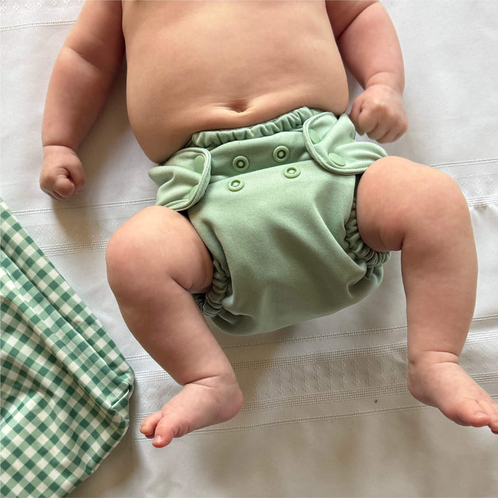 Baby wearing a green cloth diaper on a white background