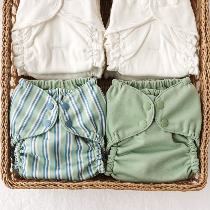 Two green cloth diapers with button closures and two stacks of Inners in a woven basket.