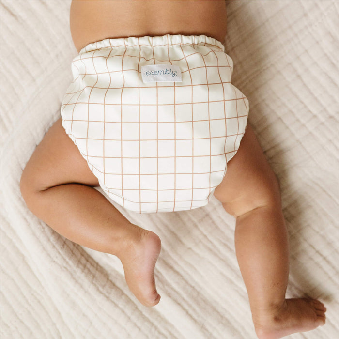 Baby wearing a Windowpane (white background with a wide, thin caramel colored grid) on a soft textured surface