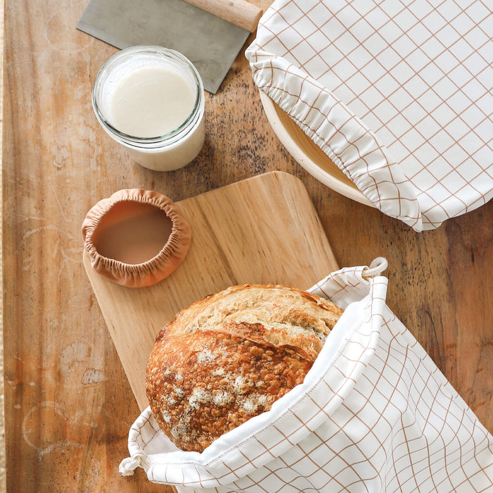 Windowpane Sourdough Set holding a boule of sourdough, covering a rising bowl, and laying next to a mason jar of sourdough starter