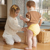 Siblings playing with wooden blocks. One of them is wearing an Esembly Outer in Buttercup (a buttery mid-tone yellow).
