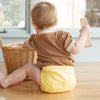 A baby playing with wooden blocks wearing an Esembly Outer in Buttercup (a soft, buttery mid-tone yellow)