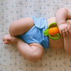 Baby laying on their back holding a carrot toy wearing an Esembly Outer in Cornflower (a soft mid-tone blue)