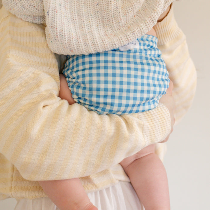 Baby in a sweater and blue Gingham Esembly Outer being held by their mom.
